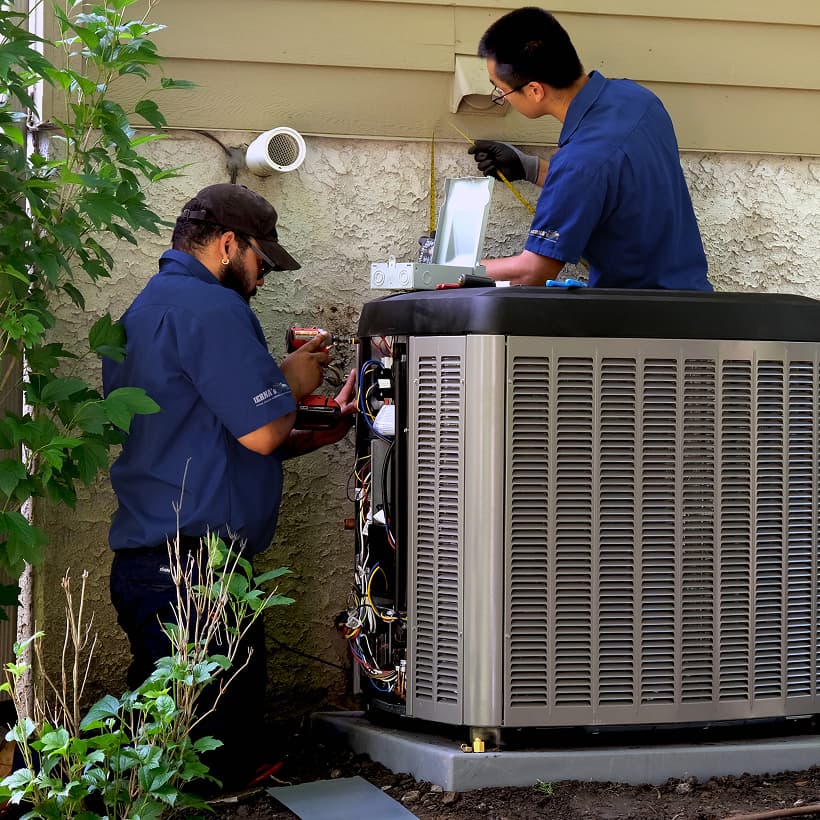 Two IERNA's HVAC technicians installing a brand-new residential outdoor air conditioning condenser unit during a home AC replacement service.