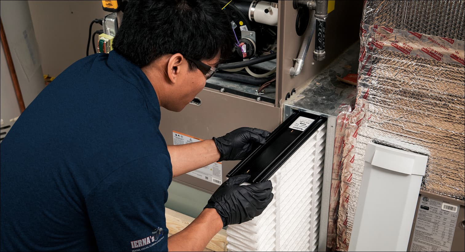 A professional IERNA's HVAC technician replacing a clean pleated air filter in an indoor air handler unit during a routine AC maintenance tune-up.